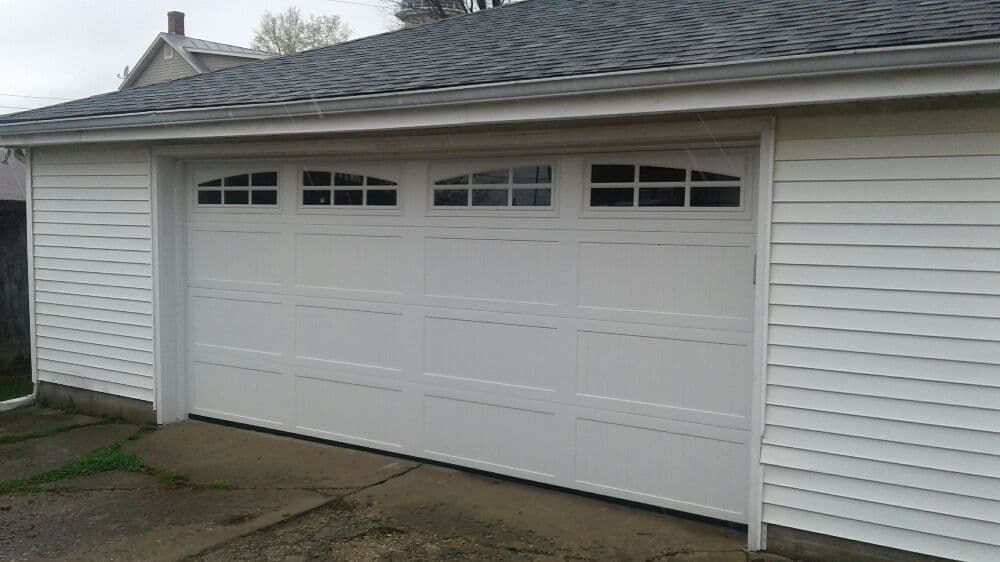 White garage door with windows, modern design, attached to a light-colored house exterior.