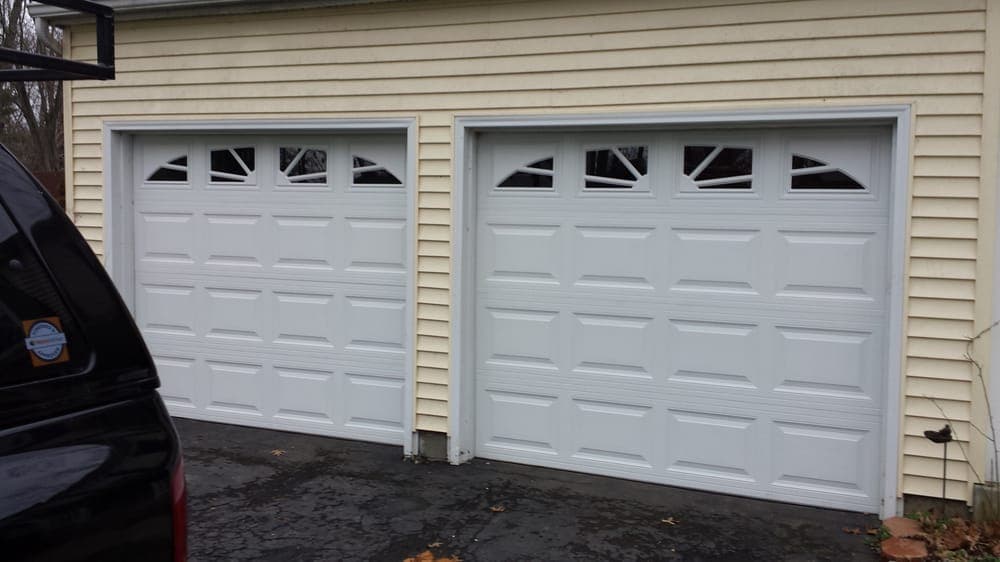 White garage doors with decorative windows, installed on a yellow house.