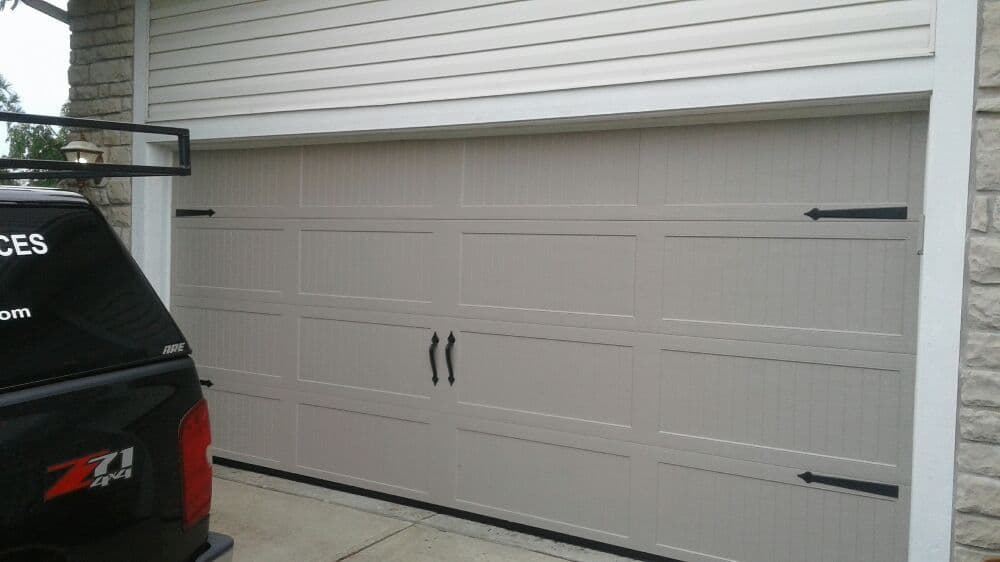 Modern beige garage door with decorative handles and arrows, adjacent to a parked truck.