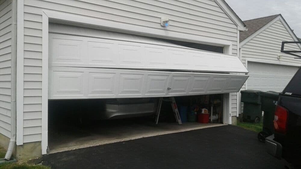 Garage door partially open, revealing a car inside, with a beige house exterior and driveway.