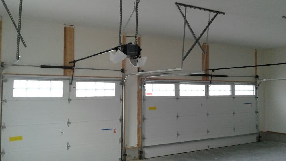 Interior view of a garage with two doors, overhead lights, and garage door openers installed.