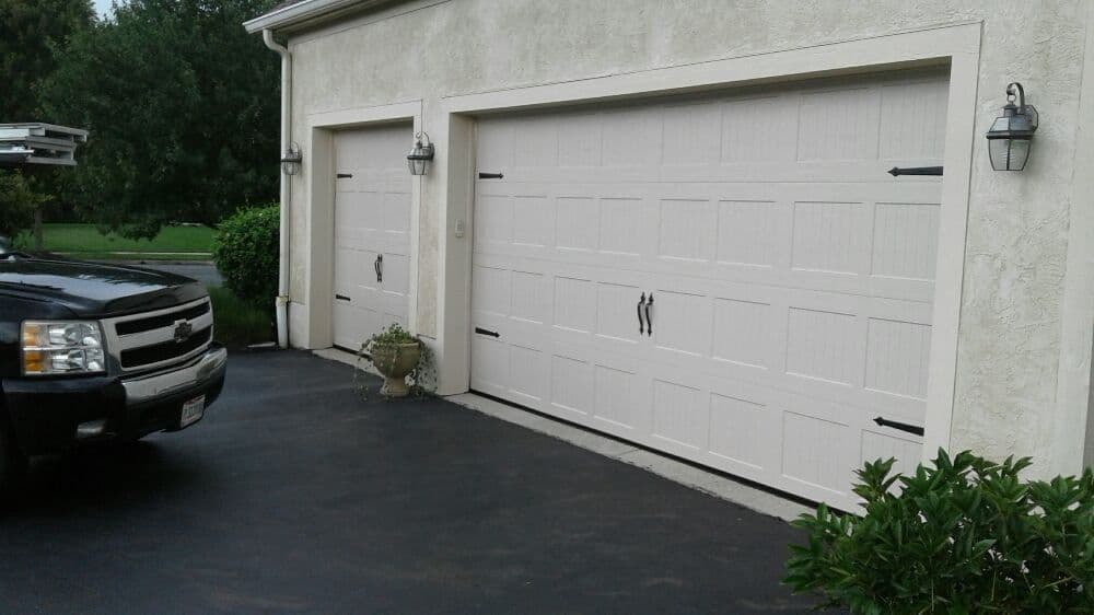 Two stylish beige garage doors with decorative hardware, next to a parked black truck.
