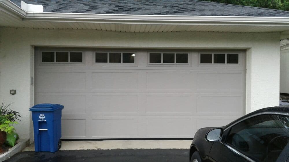Gray garage door with windows, blue recycling bin, and black car in driveway.