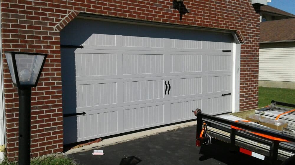 Modern white garage door on a brick home with decorative handles and outdoor lamp.