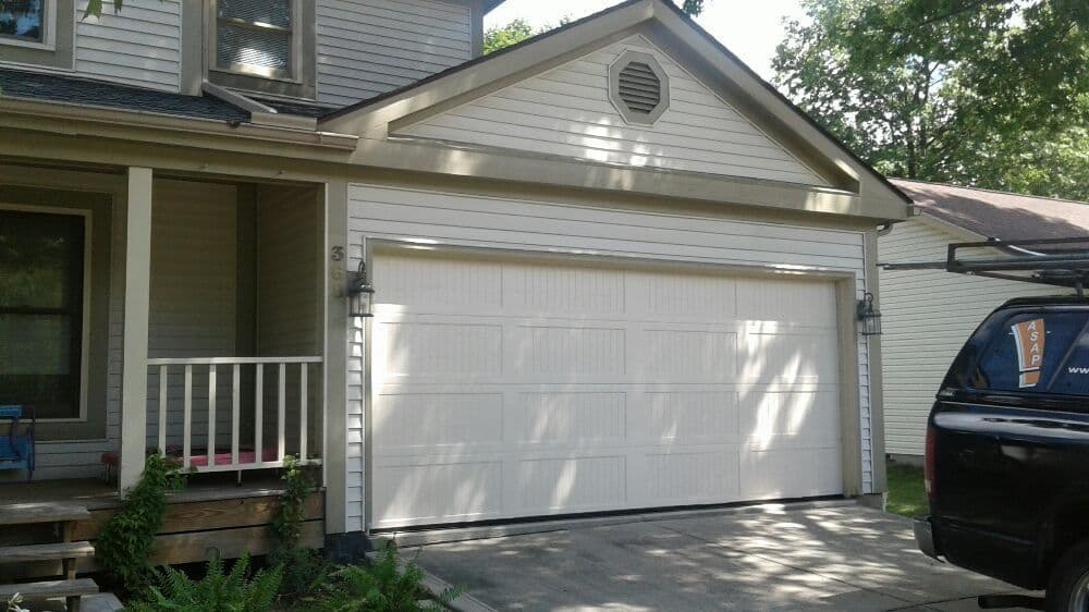 White residential garage door in front of a house with a porch and trees in the background.