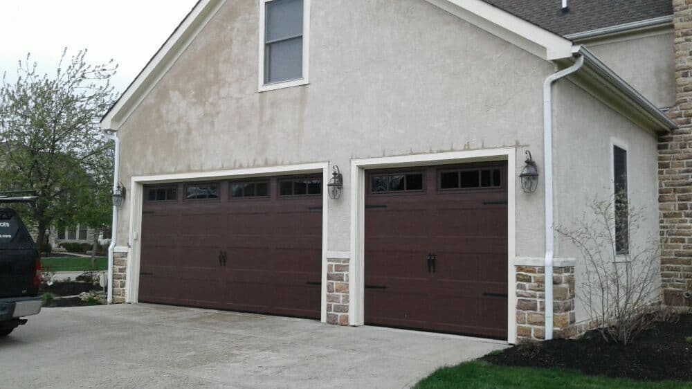 Two modern brown garage doors with windows, flanked by stone accents on a suburban home.