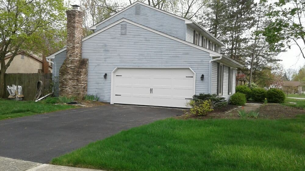 Blue residential house with a white garage door, green lawn, and chimney in a quiet neighborhood.