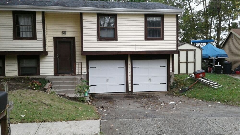Two-car garage entrance of a split-level home with a yard and nearby shed.