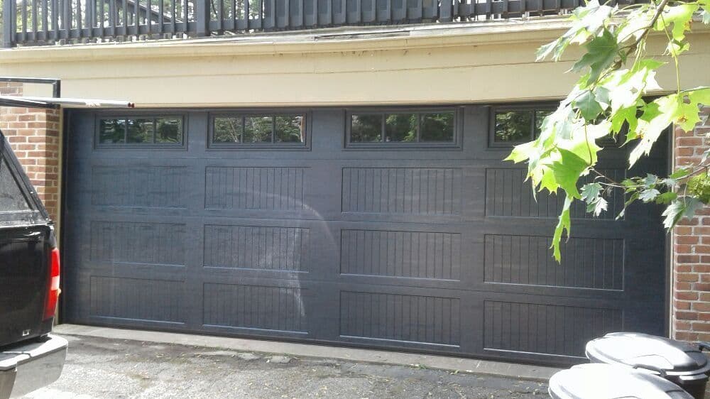 Black wooden garage door on a brick structure with windows above.