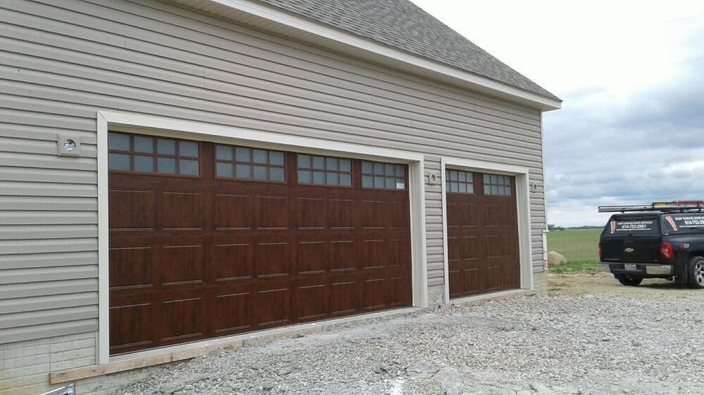 Two modern wooden garage doors on a house with a gravel driveway and cloudy sky.
