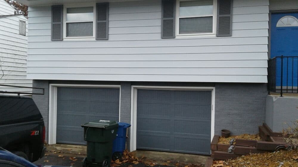 Two garage doors under a house with blue front door, surrounded by autumn leaves.