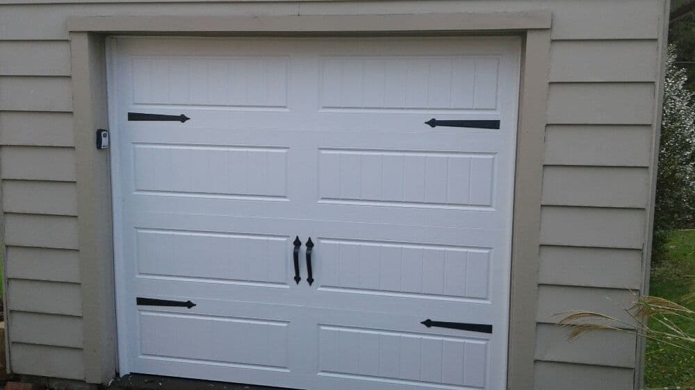 White garage door with decorative black handles and arrows on a beige siding background.