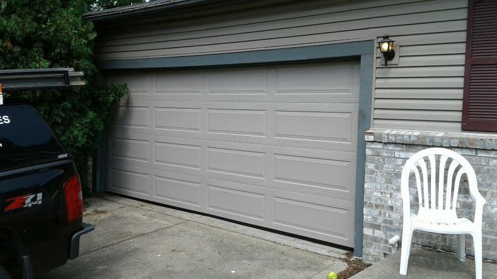 Gray garage door on a suburban home with a black truck and white plastic chair nearby.