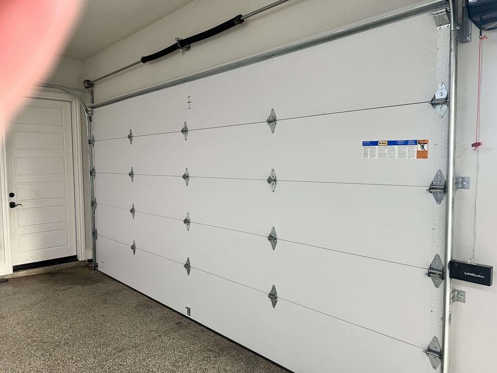 White residential garage door with vertical panels and a side door in a clean garage interior.