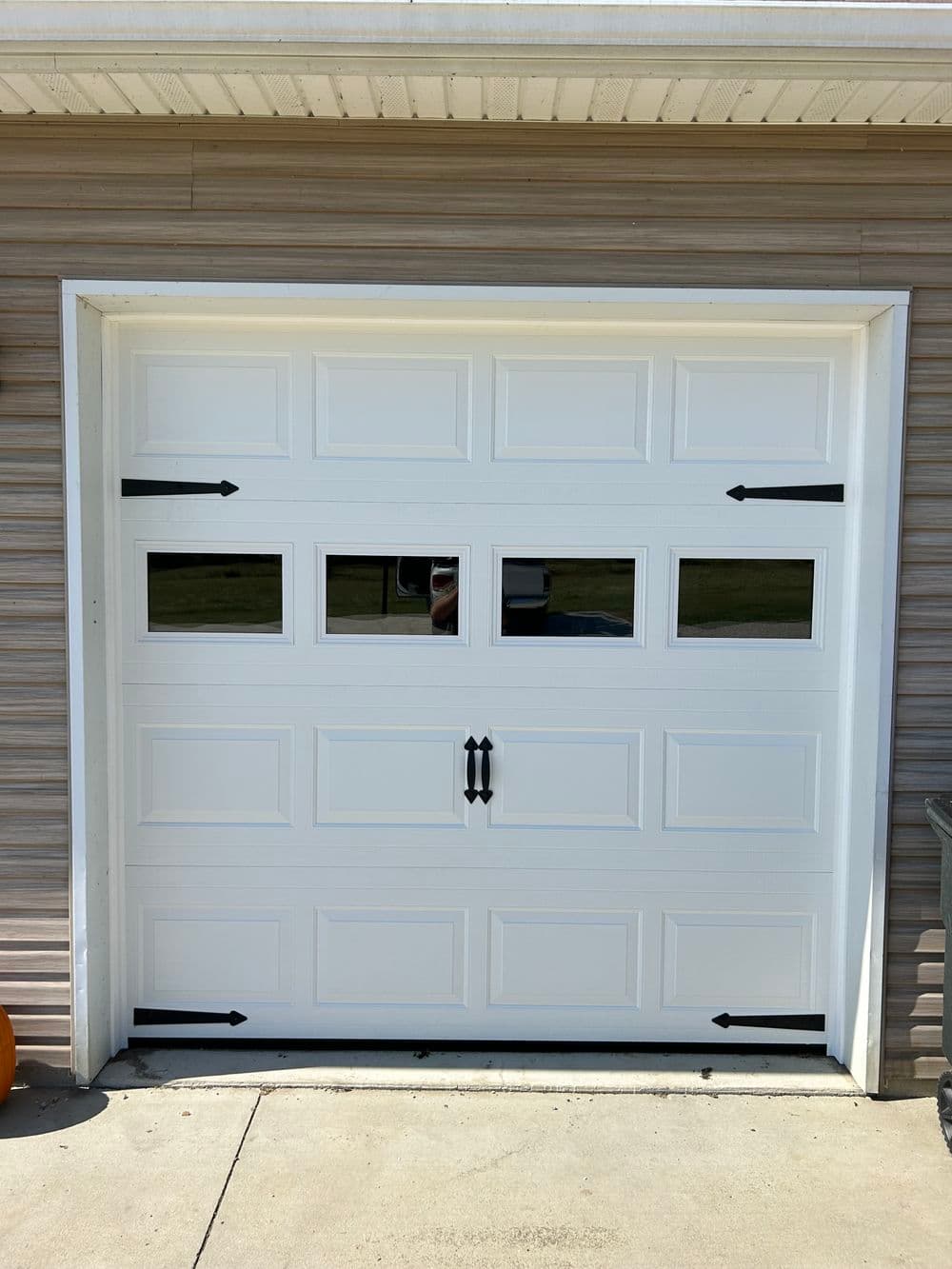 White garage door with windows and black handles against a beige building exterior.