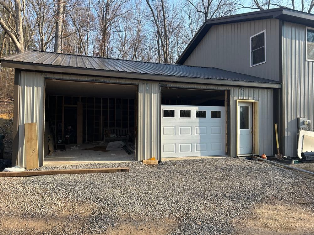 Newly constructed metal garage with unfinished interior and gravel driveway in wooded area.