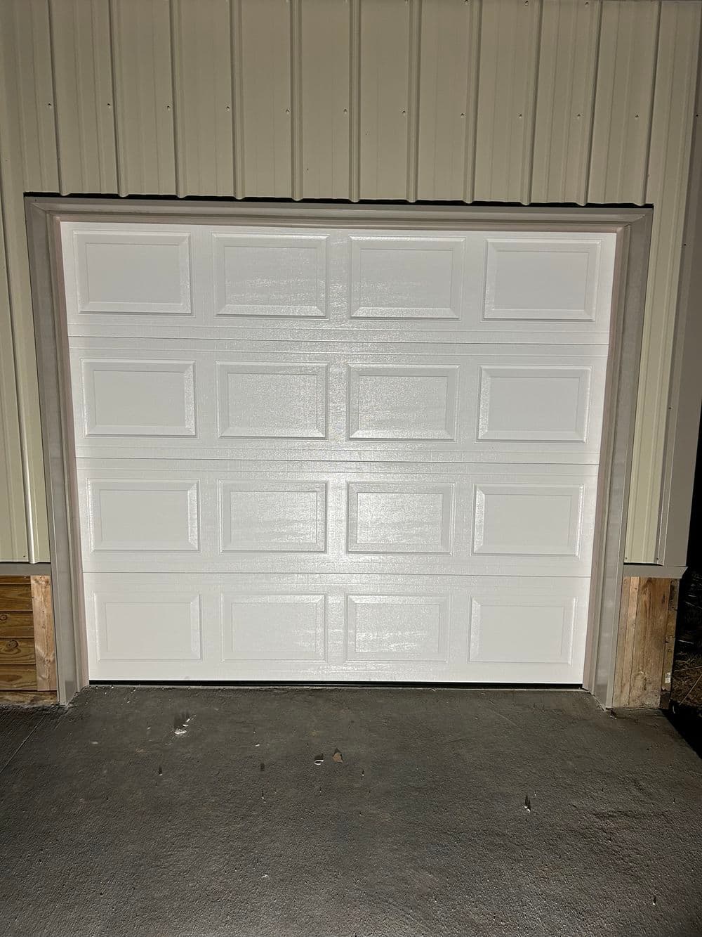 White garage door with panel design, installed in a metal building, illuminated from inside.