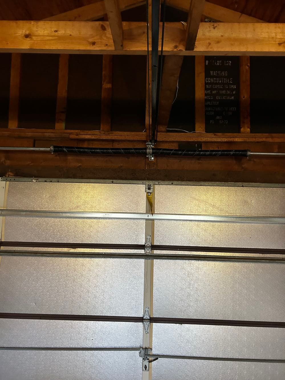 Image of a garage door mechanism with exposed wooden beams and a warning sign overhead.