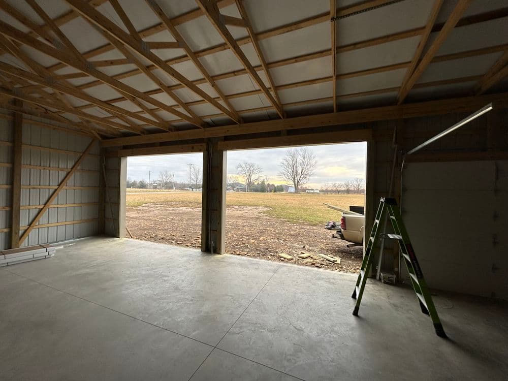 Interior view of a spacious garage with an open door, showcasing a field outside.